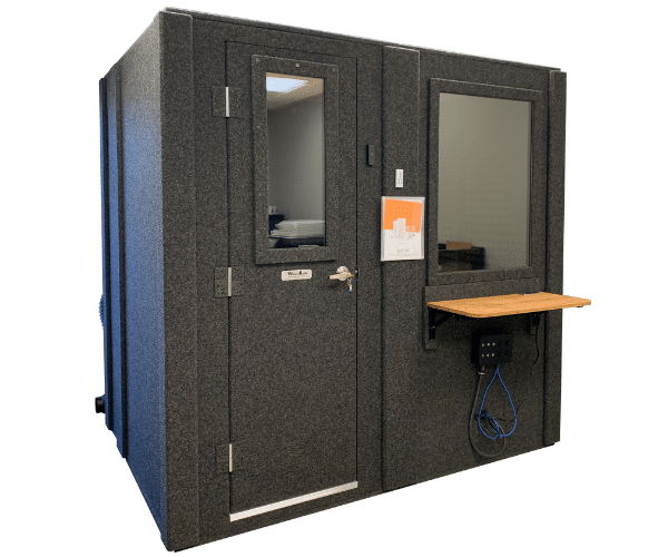 Image of a 5' x 7' Audiometric Booth for Hearing Testing. The booth features a closed door, a Multi Jack Panel attached to the exterior underneath the window, and a folding desk for testing equipment to rest on.