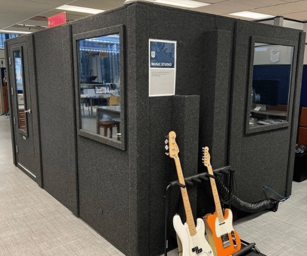 A WhisperRoom portable rehearsal booth shown from the outside with a guitar and bass next to it.