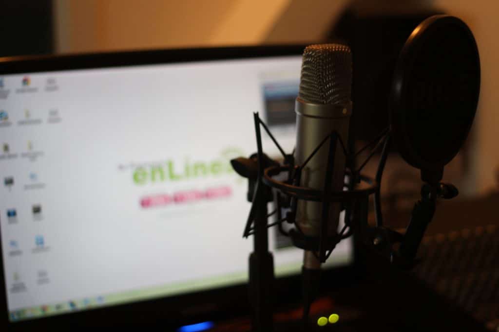 A condenser microphone in front of a turned on computer monitor