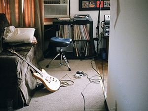 An electric guitar leaning on a bed next to a stack of records