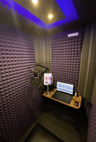 Interior of WhisperRoom with purple foam, a desk, a computer, and recording equipment