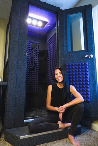 A woman sitting next to her WhisperRoom vocal booth