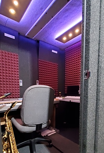 A saxophone, chair, and other instrumental gear inside of a WhisperRoom MDL 6084 S professional rehearsal booth.