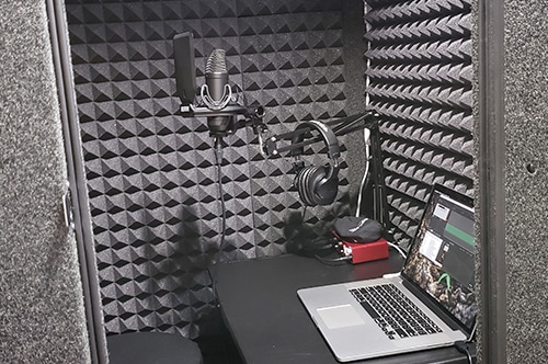 A microphone, laptop, interface, and other miscellaneous recording equipment inside of a WhisperRoom vocal booth.