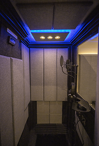 The inside of a WhisperRoom soundproof booth with acoustic panels on the wall and a condenser mic for recording.