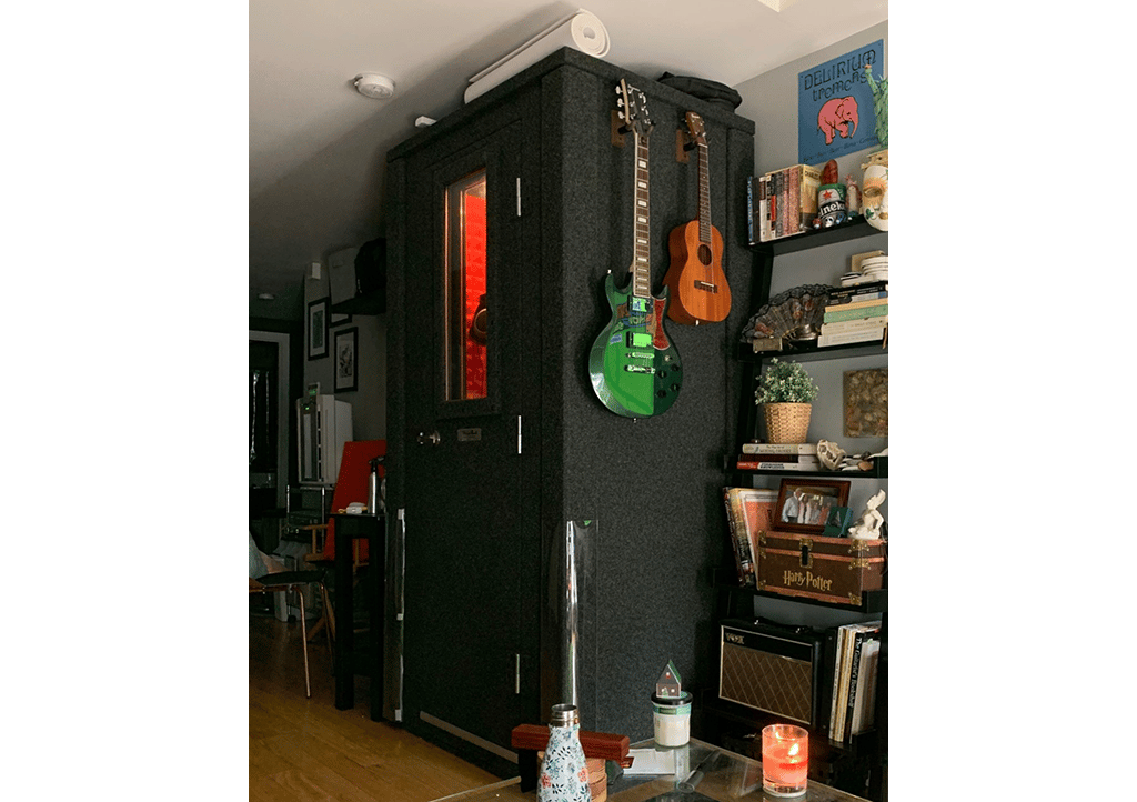 WhisperRoom MDL 4230 E shown inside of an apartment with a guitar and ukulele hanging on the side of the sound booth.