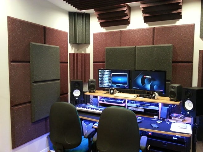 A recording studio with a variety of auralex acoustic treatment on the wall and a desk with recording equipment.