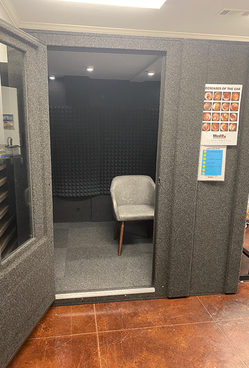 A WhisperRoom Audiology Deluxe Package is shown with the door open inside of an audiologist's office.