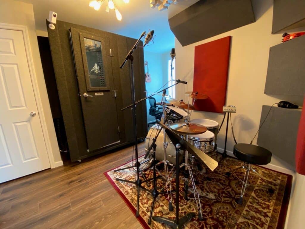 A WhisperRoom MDL 4260 S, a drum kit, and acoustic treatment behind the drums inside of a home recording studio.