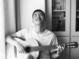 A man is smiling with his eyes shut as he enjoys playing a "C" chord on a nylon stringed guitar.