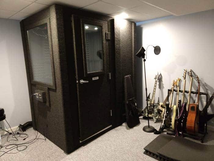 A WhisperRoom inside of a home recording studio, sitting next to a rack of guitars and a microphone.