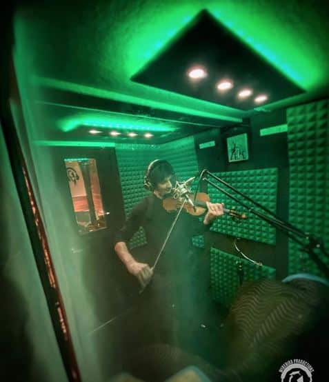 A violin player recording inside of a WhisperRoom MDL 6084 S with green lighting.