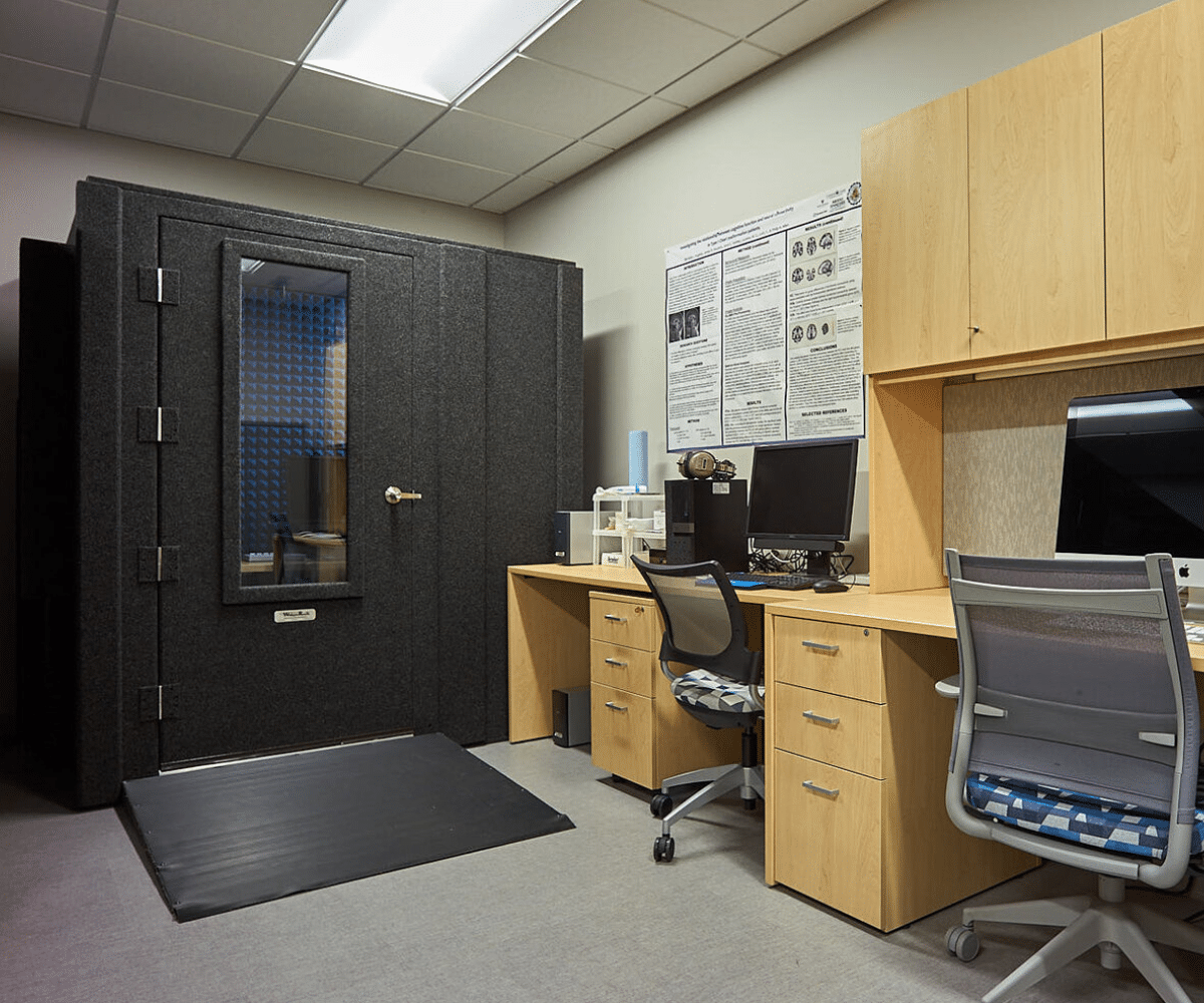 The WhisperRoom Audiology Deluxe Package showcased in MTSU's facility. The audiometric booth is visible in the center, equipped with a desk along the wall where two computers are placed. The room is designed for hearing tests and psychological assessments, providing a controlled environment for accurate measurements and evaluations.