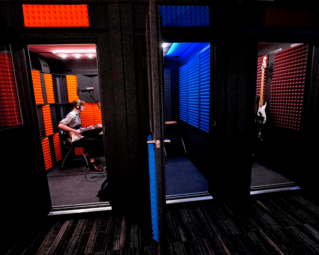 Photograph capturing a different angle of GCU's recording lab, featuring a guitarist inside one of the WhisperRooms with all unit doors open. This scene showcases active music practice and recording within the sound isolation booths.