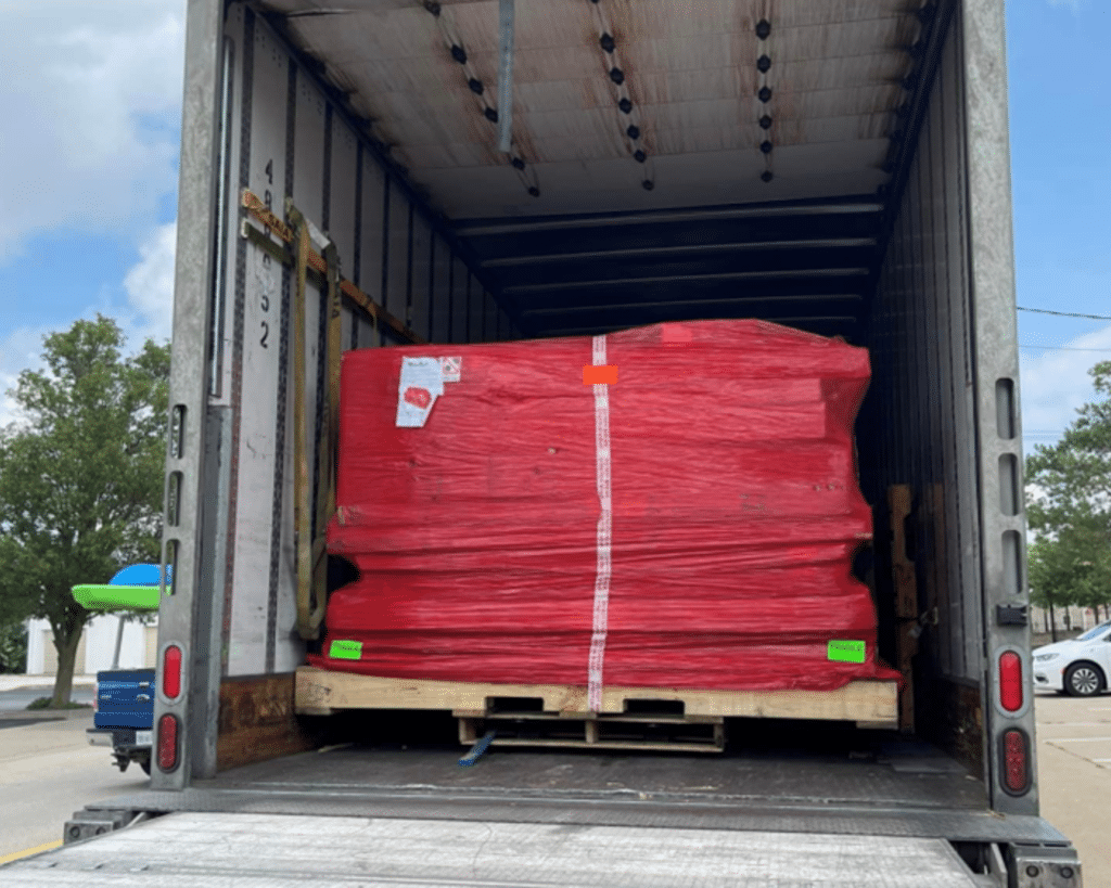 Photograph capturing a palletized WhisperRoom order loaded onto the rear of an open semi-truck for transportation.